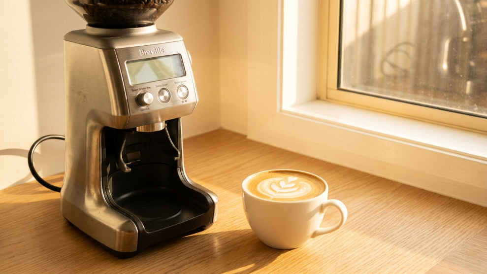 Electric burr coffee grinder on an Australian kitchen counter with flat white cup.