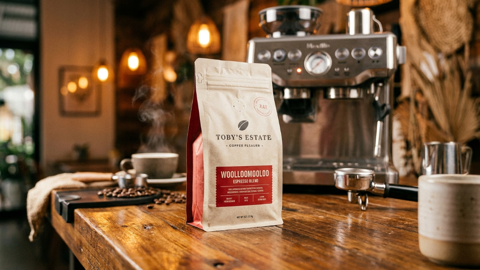 Toby's Estate Woolloomooloo Espresso Blend specialty coffee bag on a wooden surface with espresso machine in background