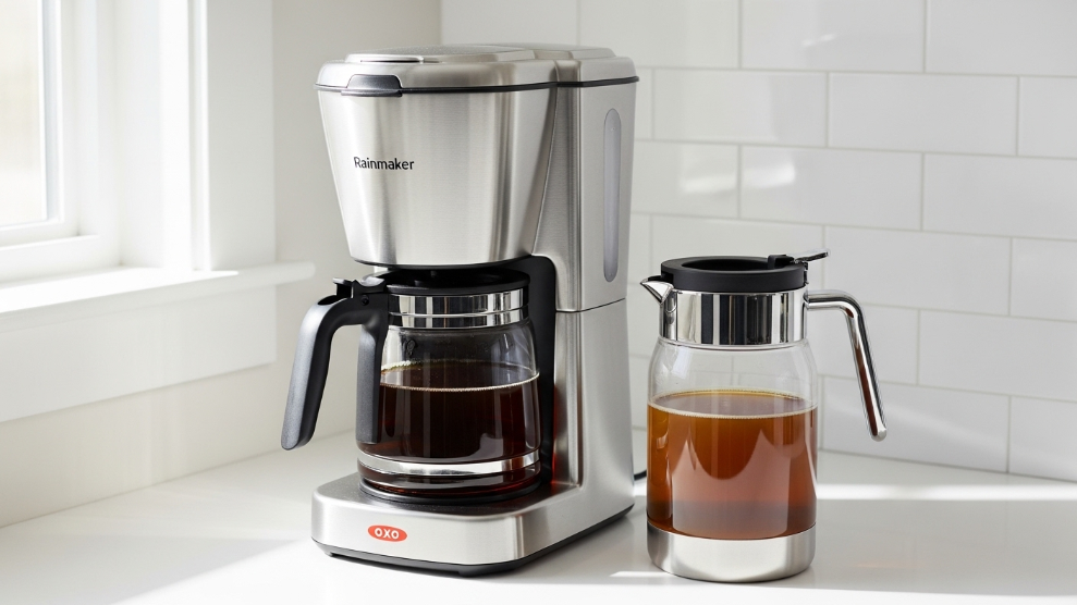 OXO Brew 9-Cup drip coffee maker in stainless steel with Rainmaker showerhead visible and thermal carafe of brewed coffee beside it